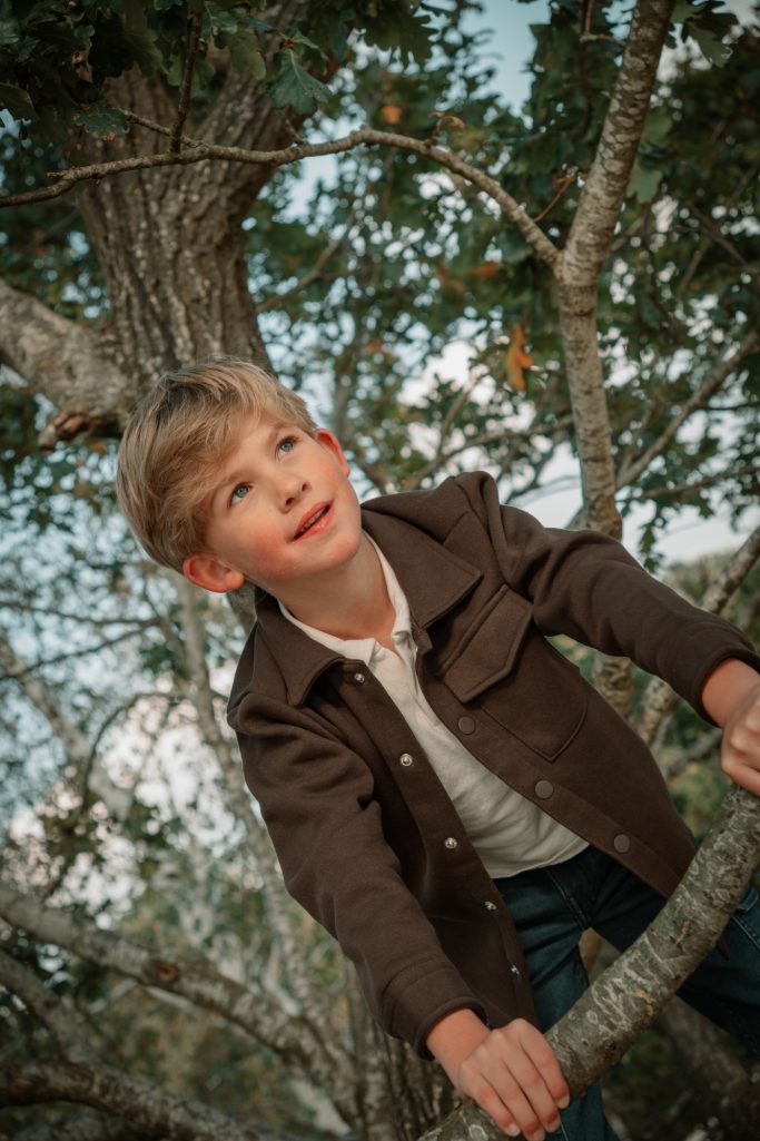 Spelen in het bos Jongen kijkt omhoog tussen de bomen tijdens een kinderfotoshoot in de buitenlucht.
